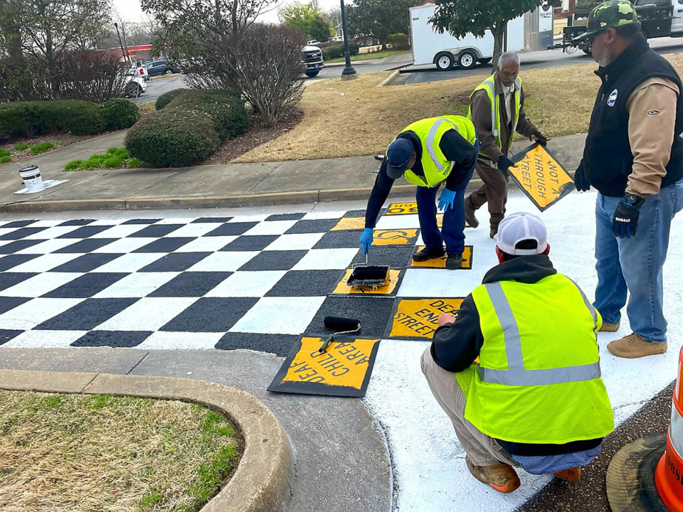 <strong>City workers Matt Crabb (back to camera), Alton Williford, Jimmy Ray Bougard and Mark Tate lay old street signs onto asphalt painted white in order to create the checkerboard flag look to honor Olive Branch native son Ricky Stenhouse Jr., winner of the Daytona 500.</strong> (Credit Cole Fesmire)