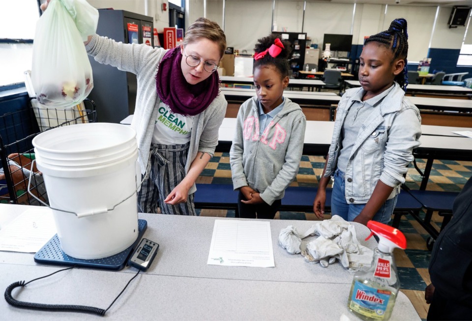 <strong>Emma Simmons (left) with Clean Memphis along with Scenic Hills Elementary School fourth graders Zoey Morton,10 (middle) and Emani Lacy, 9, (right) weigh partially eaten apples for a food waste audit on Wednesday, March 22, 2023.</strong> (Mark Weber/The Daily Memphian)