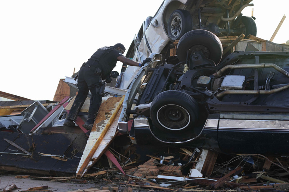 <strong>A sheriff's deputy climbs onto a pile of wind-tossed vehicles to search for survivors or the deceased at Chuck's Dairy Bar in Rolling Fork, Miss., March 25.</strong> (Rogelio V. Solis/AP Photo)