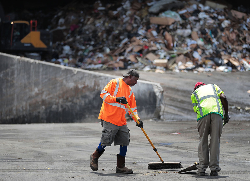 <strong>Darren Gwyn (left) and Charles McKinney who work the tarping station at the Waste Connections of Tennessee facility on Brooks Road clean up some stray garbage off one of the trucks.</strong> (Jim Weber/The Daily Memphian file)