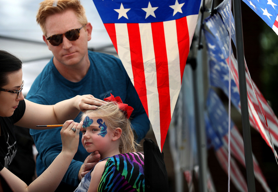 <strong>Todd Sparks helps face painter Michelle Chambers keep his daughter Marjorie, 3, still as she gets adorned after the annual Fourth of July parade in the Cooper-Young neighborhood on July 4, 2019.</strong> (Jim Weber/Daily Memphian)