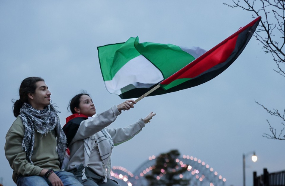 <strong>Dodi Imam and Marcela Espinoza wave a Palestinian flag as a protest in Downtown Memphis wanes Saturday, Feb. 3. From their vantage point on Main Street just south of Poplar Avenue, the Hernando DeSoto Bridge shimmers in the background.</strong> (Patrick Lantrip/The Daily Memphian)