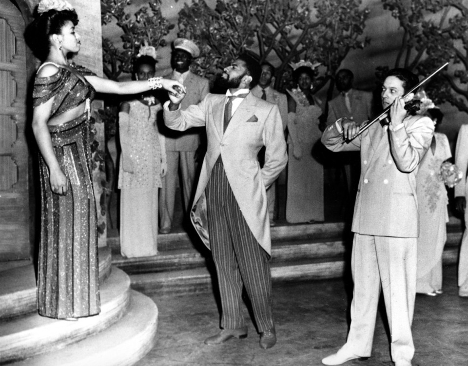 <strong>Muriel Smith, left, in the title role Carmen Jones, gives her hand to P. Jay Sidney, playing Mr. Higgins, the owner of the Meadowlawn Country Club, the setting for Act II, Scene I, in October 1943. The violinist is Everett Lee. "Carmen Jones" is the Broadway version of Bizet's opera.</strong> (AP File Photo)
