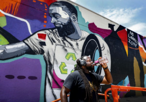 <strong>Local artist Jamond Bullock takes a long swig of a refreshing drink on a hot July day, while completing a mural in Frayser, his home neighborhood. The mural is part of an initiative with the UrbanArt Commission in Memphis.</strong> (Mark Weber/Daily Memphian).