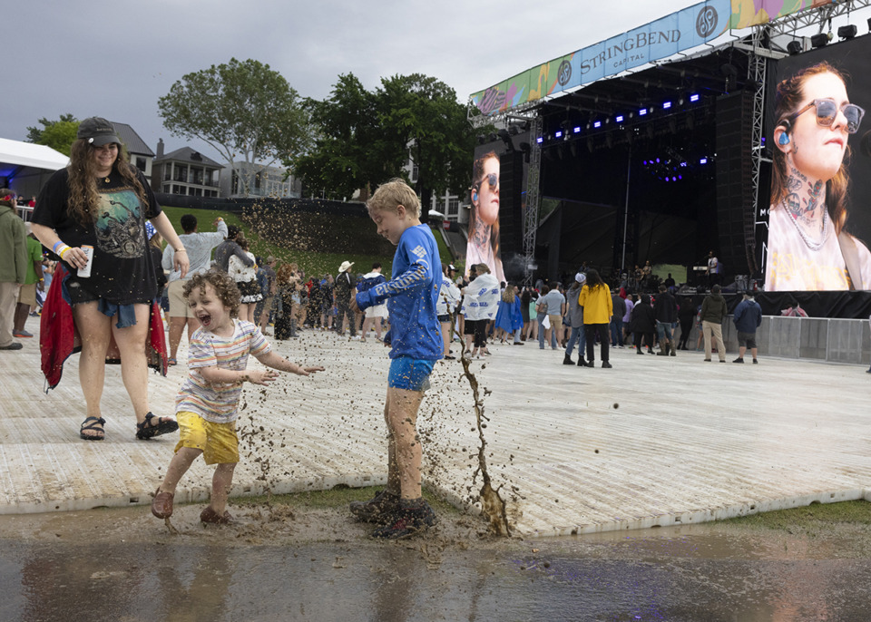 <strong>Mackenzie Carson, far left, watches youth, left to right, Henry and Rhett Fisher play in rain and mud puddles during the final day of Riverbeat Music Festival at Tom Lee Park in Downtown Memphis on Sunday, May 5, 2024.</strong> (Ziggy Mack/Special to The Daily Memphian)