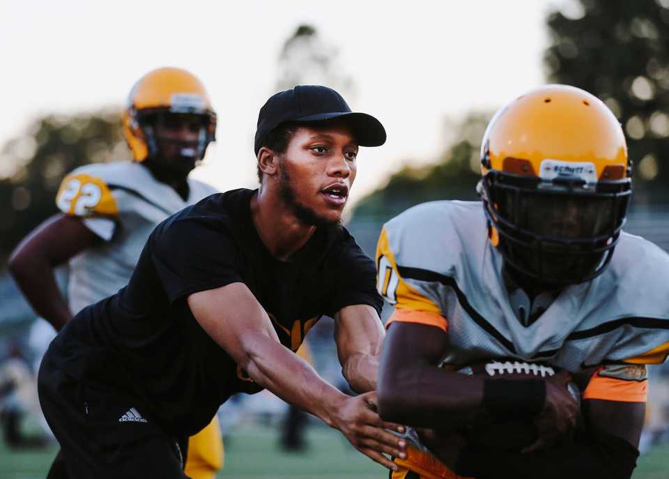 <strong><span>Memphis Academy of Health Sciences</span> assistant coach Cedric Miller Jr. (left) hands off the football to one of his running backs during practice. Miller is one of a young group of MAHS assistant coaches who all played high school ball together at Southwind.</strong> (Houston Cofield/Daily Memphian)