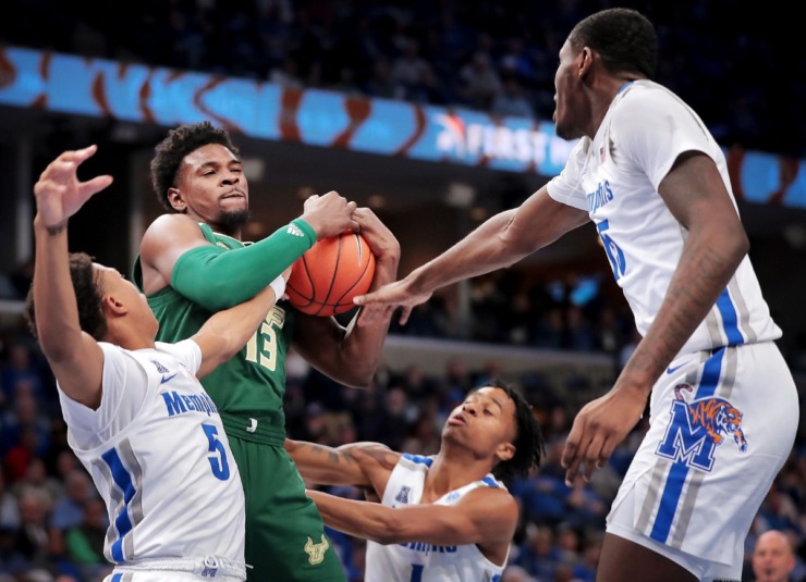 <strong>Bulls forward Justin Brown pulls down a rebound under pressure by University of Memphis guard Boogie Ellis (5), Tyler Harris (center) and Lance Thomas (right) during the Tigers' game on Feb. 8, 2020, against USF at FedExForum in Memphis.</strong> (Jim Weber/Daily Memphian)