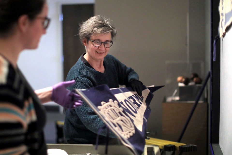 <strong>Tammy Braithwaite (right) and Jestein Gibson hang a circa-1912 pennant on the wall on Friday, March 6, at the Pink Palace Museum's new exhibit on the history of the University of Memphis men's and women's basketball programs.</strong> (Patrick Lantrip/Daily Memphian)