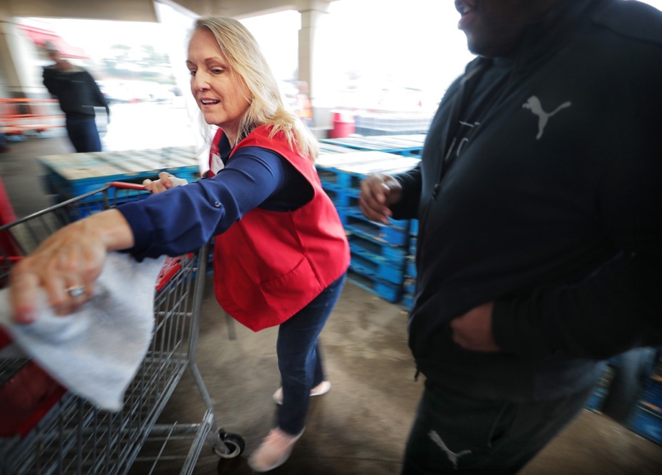 <strong>Costco employee Jodie Bowden disinfects grocery cart handles for customers as the enter the busy Costco on Germantown Parkway where management attempts to comply with federal social distancing guidelines by allowing 10-20 customers into the store periodically, a policy designed to control checkout lines and crowding.</strong> (Jim Weber/Daily Memphian)