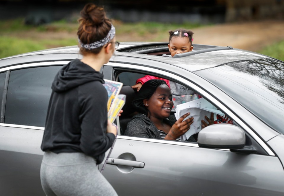<strong>Autumn Robison, 2, pears out from a sunroof as her aunt Carlesha Chearie (bottom) grabs classwork from 1st grade teacher Tylor Beardall (left) at KIPP Memphis Preparatory Elementary school on Friday, March 20, 2020.</strong> (Mark Weber/Daily Memphian)
