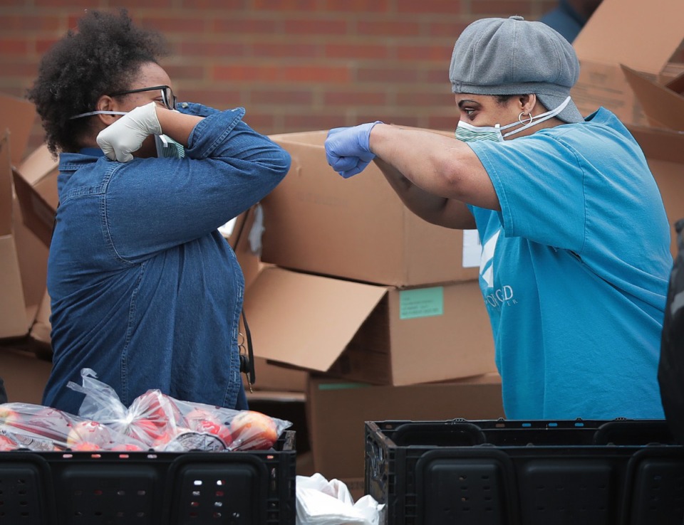 <strong>Marisa McCracklin (left) and Vernetta Johnson experiment with new ways to high-five as members of the Pursuit of God Church in partnership with Life Church, Bellevue Baptist and Mid-South Food Bank assemble some 250 food baskets to give away to those in need on March 20, 2020 at Pursuit of God Church in Frayser.</strong> (Jim Weber/Daily Memphian)