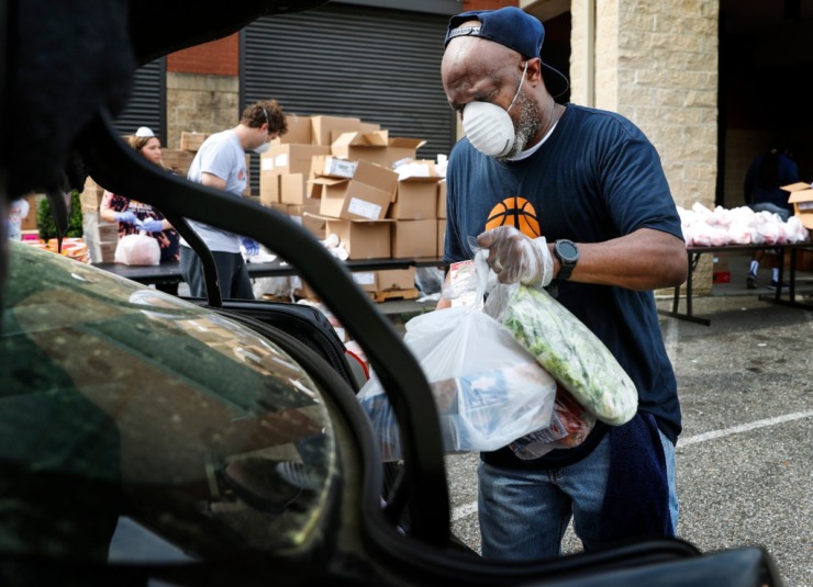 <strong>Memphis Athletic Ministries volunteer Lindell Bonner places fresh vegetables and fruit in a car trunk during a drive-through food distribution on Friday, March 27. Nearly 12,000 pounds of food and 200 14-day food boxes were handed out to families that waited in lines reaching more than a mile long.</strong> (Mark Weber/Daily Memphian)