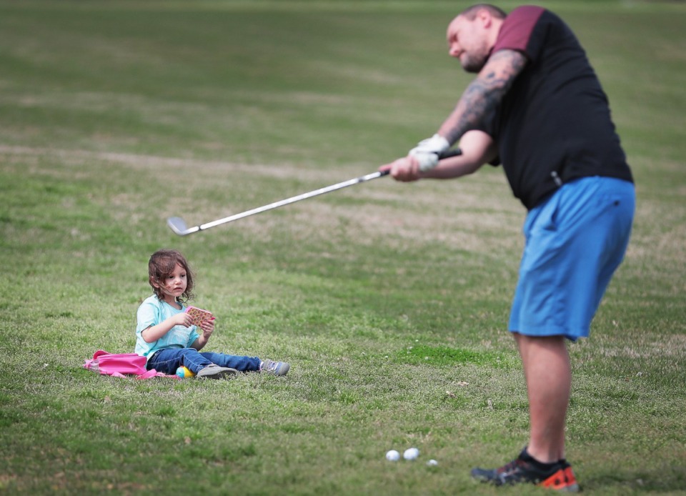 <strong>Leilani Ratts, 2, keeps herself entertained with video games while her father Andrew Ratts practices his chip shot at the Overton Park golf course on March 23, 2020.</strong> (Jim Weber/Daily Memphian)