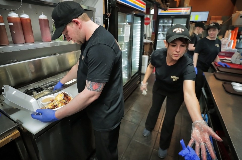 <strong>Chris Wooley (left) makes barbecue nachos while Para McGregor keeps everything disinfected during a busy lunch rush at the Baby Jacks BBQ takeout window on April 3, 2020. Baby Jacks is busier than ever as the restaurant adapts to the pandemic by delivering large numbers of boxed lunches to places like area hospitals.</strong> (Jim Weber/Daily Memphian)