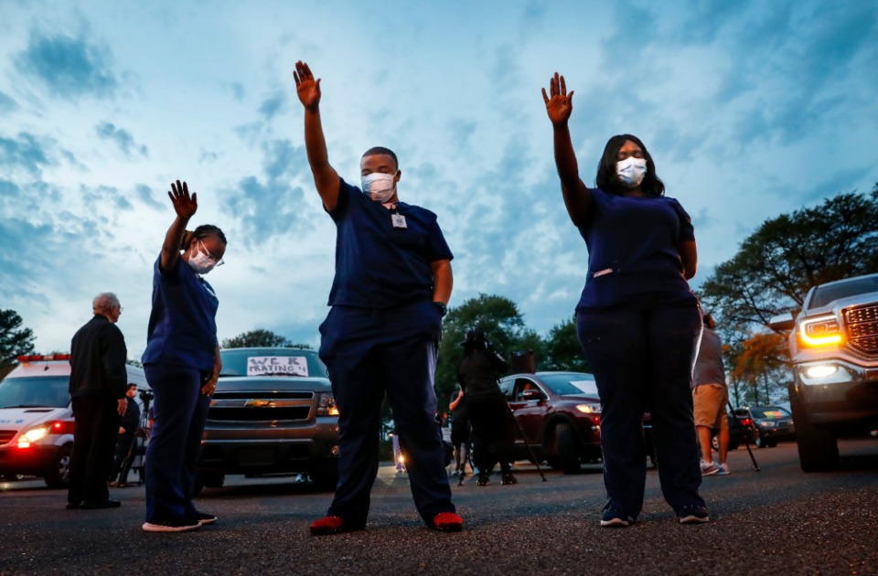 <strong>St. Francis Hospital-Memphis nurses, including Deonta Buck (middle) raise their hands in praise while attending a prayer vigil for patients and staff in the hospital parking lot on Monday, April 6, 2020.</strong> (Mark Weber/Daily Memphian)