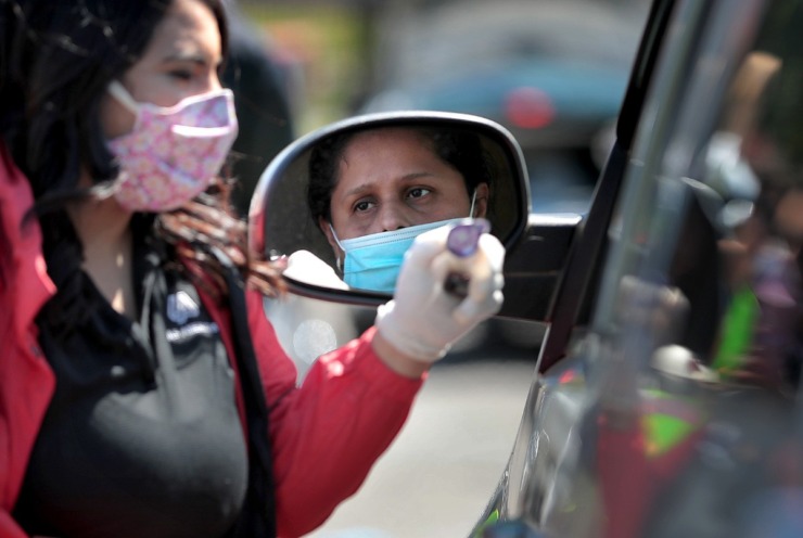 <strong>Damaris Diaz (left) hands out self-contained communion cups as some 80 volunteers from Las Americas and Nueva Direccion Church rush to distribute food for 1,000 families on April 10, 2020, from the Mid-South Christian College campus.</strong> (Jim Weber/Daily Memphian)