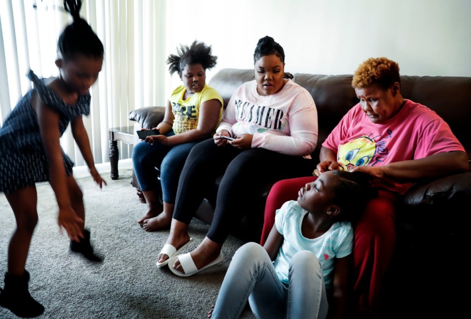 <strong>Beverly Robinson (right, pink shirt) works on the hair of her daughter Kensley Robinson, 10, as her other daughter Kentara Robinson, 17, (middle) and granddaughters Krystal Cole, 8 (second left), and Kelsey Robinson, 5, play on their phones or dance in their Hickory Hill apartment on Wednesday, April 15, 2020. In Shelby County, 71% of those who test positive for COVID-19 are African Americans.</strong> (Mark Weber/Daily Memphian)