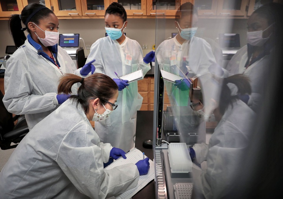 <strong>Medical technicians Jasmine Becton (left), Lanthanh Nguyen and Calisha Beauregard train on a new piece of equipment between processing patient samples at UTHSC's Coronavirus testing lab in the Hamilton Eye Center on April 16, 2020.</strong> (Jim Weber/Daily Memphian)