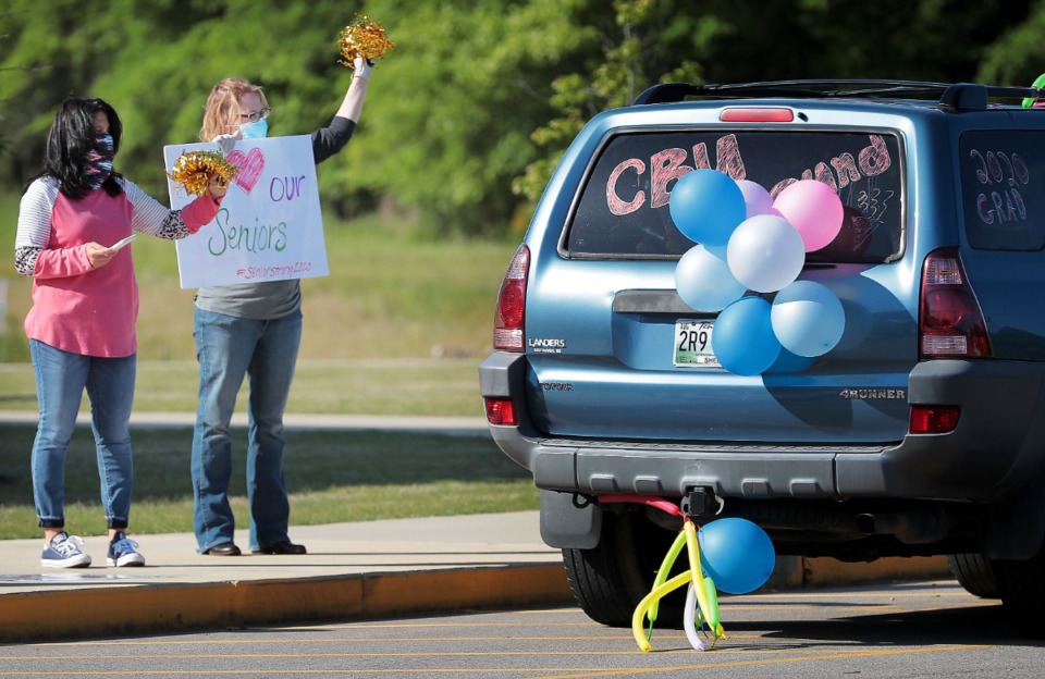 <strong>Melissa Wilkinson (left) and Julie Johnson cheer for Collierville High School graduates driving through to pick up caps and gowns at the school on May 7, 2020. Collierville teachers, staff and PTSO members turned out to celebrate with the seniors.</strong> (Jim Weber/Daily Memphian)