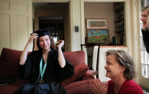 <strong>Grace Siler, 2020 valedictorian of the Memphis College of Art, moves her tassel across to the other side of her cap after her name is announced on the TV set during the school's final graduation ceremony on May 9, 2020, which had to be video broadcast online because of COVID-19. Siler and MCA Vice President of Academic Affairs Cathy Wilson (right) watched the video ceremony with family members during a small graduation party in East Memphis.</strong> (Jim Weber/Daily Memphian)
