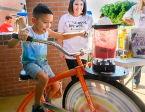 <strong>Chris Arredondo, first grader, pedals to make a smoothie with the help of Beth Ross at the Y on the Fly event with the Memphis-MidSouth YMCA and UnitedHealthcare last September.</strong> (Greg Campbell/Daily Memphian file)