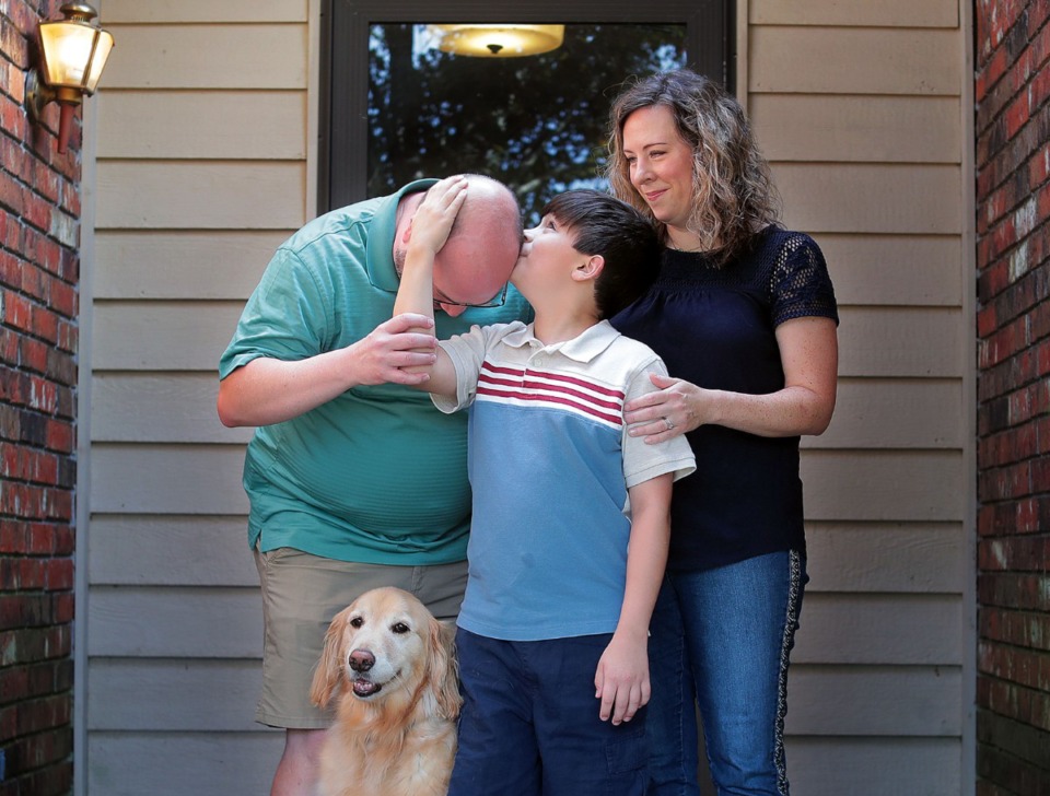 <strong>Sam Mason couldn't resist giving his father, Eric, a kiss when he bent down to get the attention of their dog, Tabor, during a family portrait with his mother, Cathy, outside their Bartlett home on Friday, July 3. Sam, who is autistic, receives $1,300 from the state of Tennessee to pay for speech therapy, but if that revenue stream dries up, the Masons may be forced to make the difficult choice of paying for Sam's speech therapy or Eric's insulin.</strong> (Patrick Lantrip/Daily Memphian)