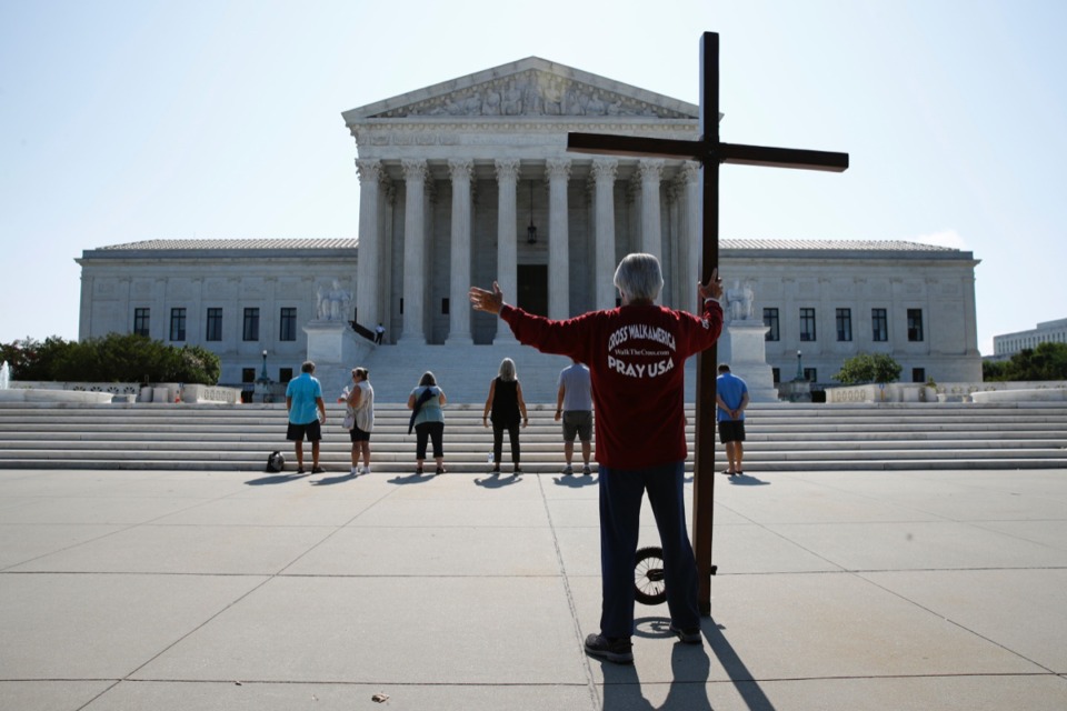 <strong>Tom Alexander holds a cross as he prays prior to rulings outside the Supreme Court on Capitol Hill in Washington, Wednesday, July 8, 2020. The Supreme Court is siding with two Catholic schools in a ruling that underscores that certain employees of religious schools, hospitals and social service centers can&rsquo;t sue for employment discrimination.</strong> (Patrick Semansky/AP)