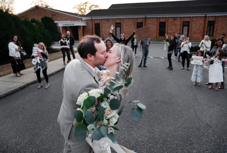 <strong>Married couple Holly Whittle and John Steinert kiss in front of their cheering friends who surprised them in the parking lot after their wedding on Saturday, March 21, 2020 at St. Louis Catholic Church. The couple had to pare down their wedding after social distancing was strongly encouraged to decrease the spread of the coronavirus.</strong> (Mark Weber/Daily Memphian)