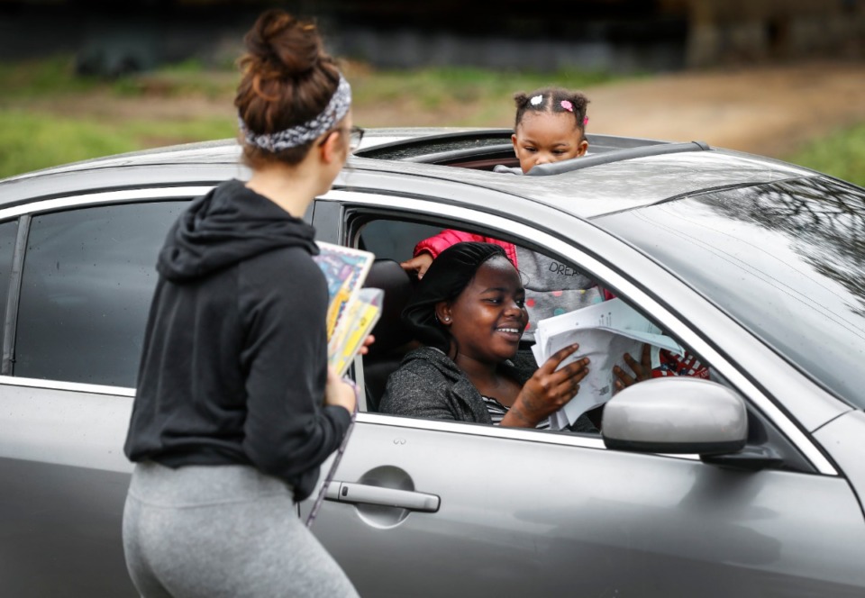 <strong>Autumn Robison, 2, peers out from a sunroof as her aunt Carlesha Chearie (bottom) grabs classwork from first grade teacher Taylor Beardall (left) at KIPP Memphis Preparatory Elementary school on March 20, 2020.</strong> (Mark Weber/Daily Memphian file)