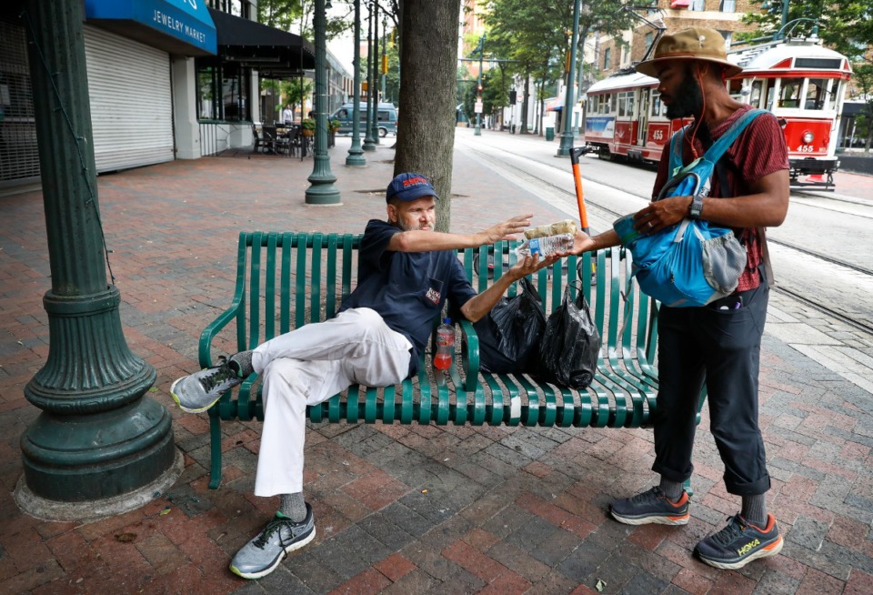 <strong>Chauncey Foster (right) offers water and burritos to Rob Branan Thursday, July 1, 2021 on Main Street. Foster is walking from Virginia Beach to San Francisco to promote the nonprofit We Grow Eco.</strong> (Mark Weber/The Daily Memphian)