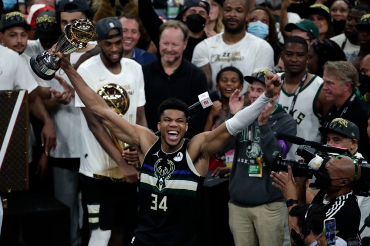 Milwaukee Bucks forward Giannis Antetokounmpo (34) celebrates with the MVP trophy, as teammates hold the championship trophy, after defeating the Phoenix Suns in Game 6 of basketball's NBA Finals Tuesday, July 20, 2021, in Milwaukee. The Bucks won 105-98. (AP Photo/Aaron Gash)
