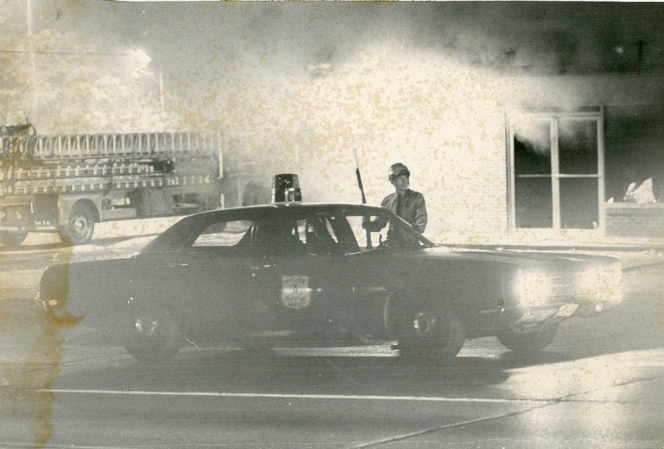 <strong>A Memphis Police officer on patrol during the violence that followed the funeral of Elton Hayes in October 1971. The smoke is from a nearby fire inside a business with a fire truck nearby.</strong> (Special Collections Department, University of Memphis Libraries)